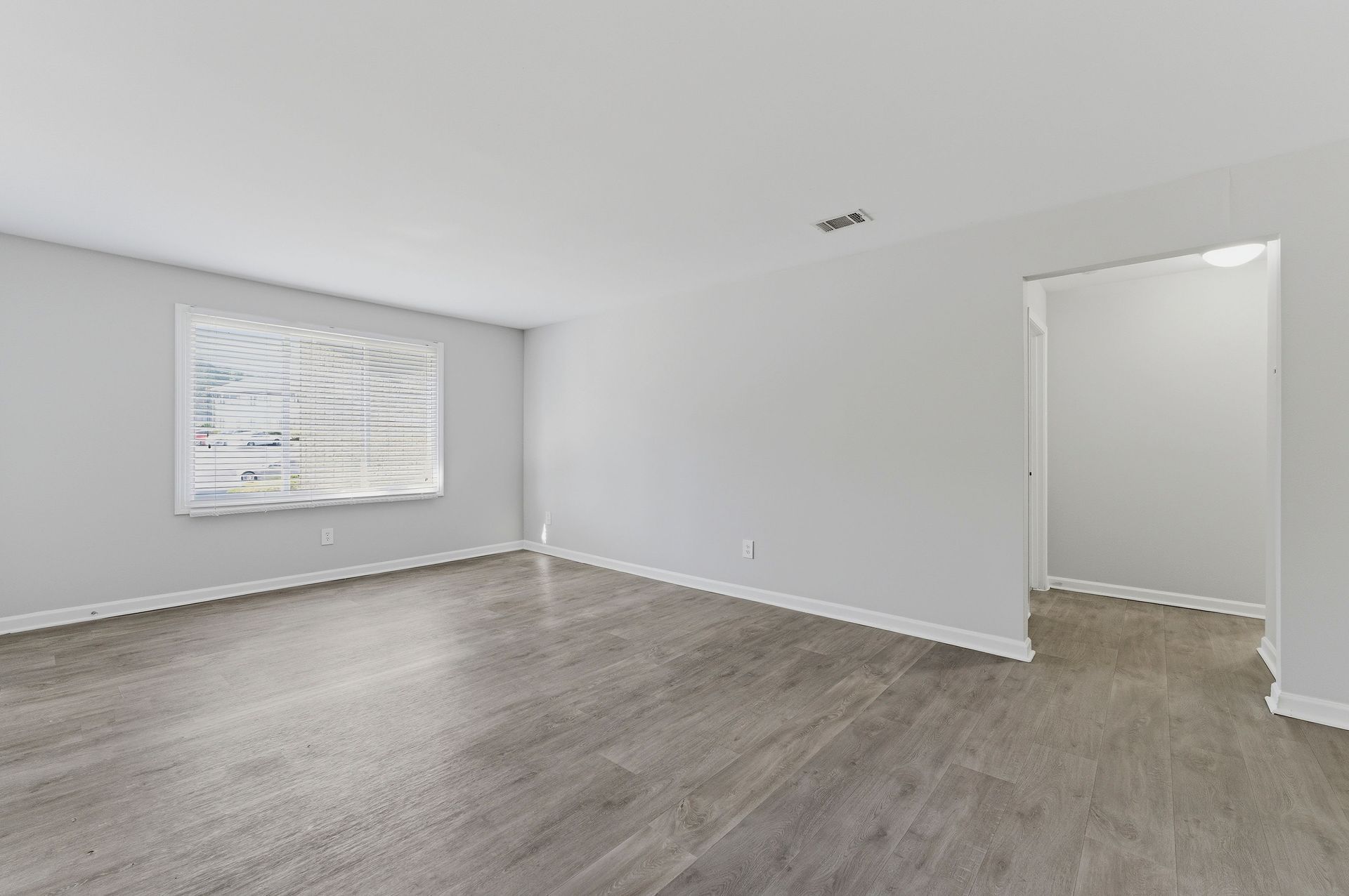 Empty white room with gray wood floors and an open doorway, lit by natural light.