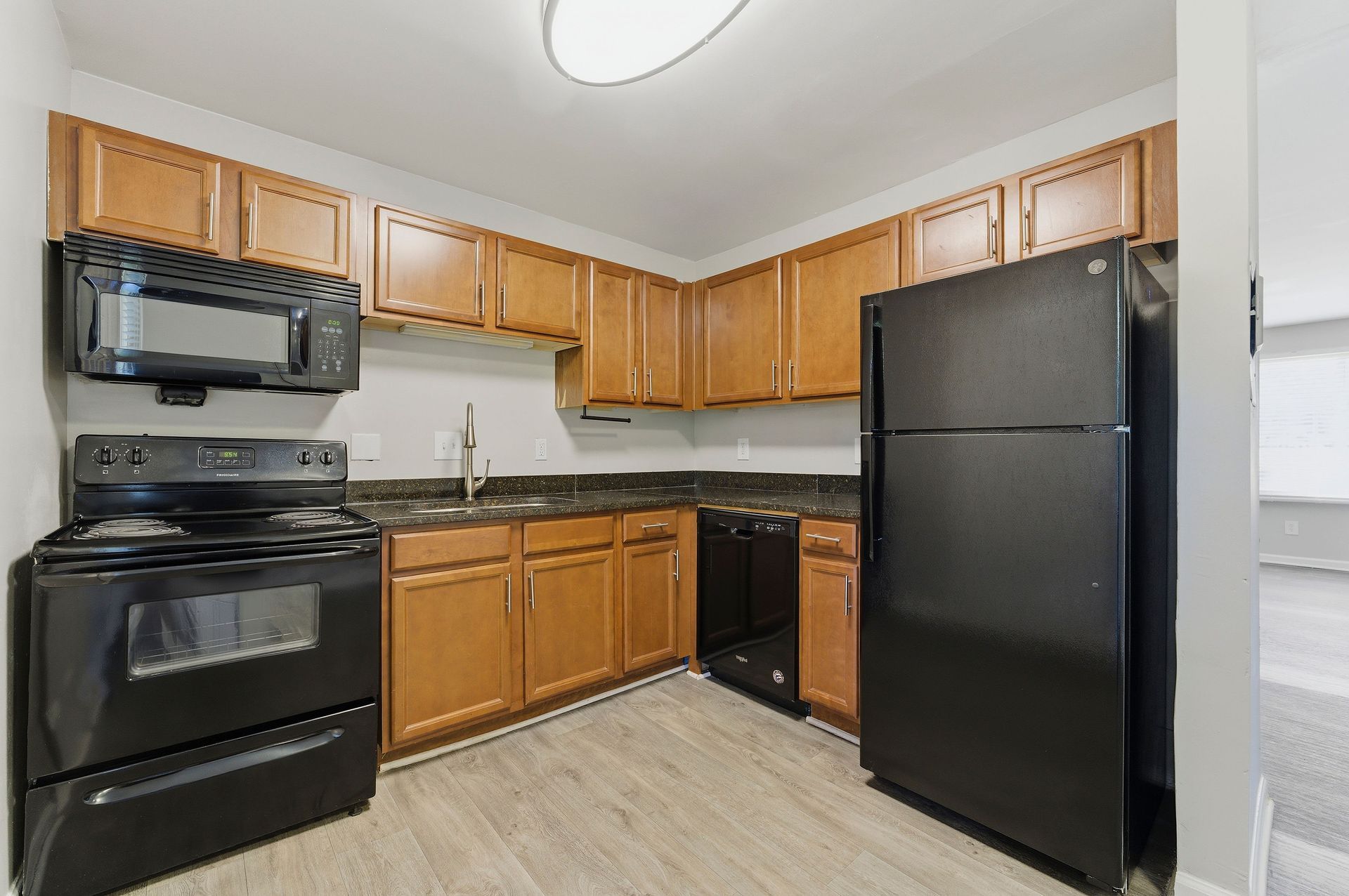 Compact kitchen with black appliances, wood cabinets, and light flooring