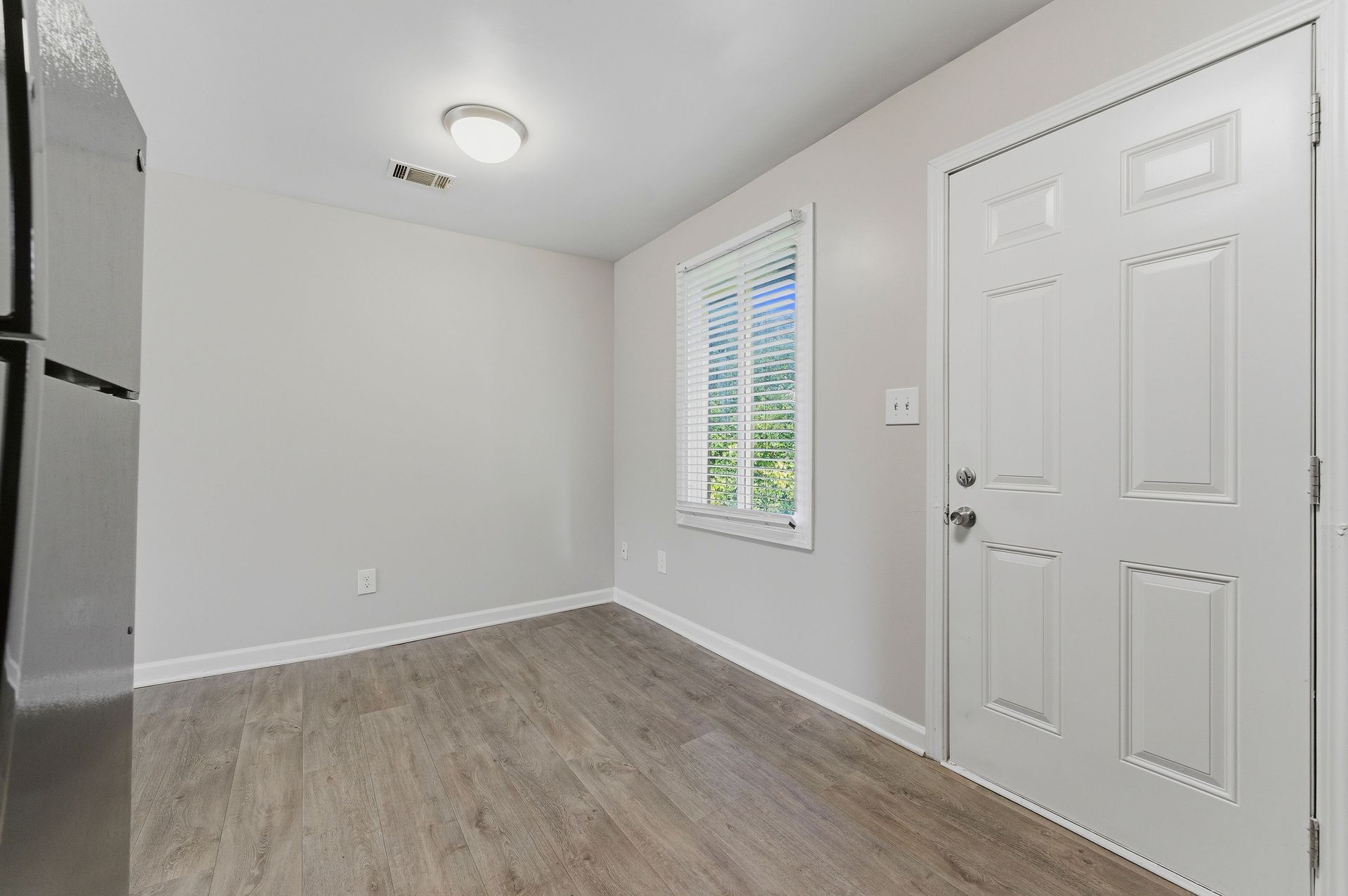 Empty white entryway with wood flooring, a window, and a front door