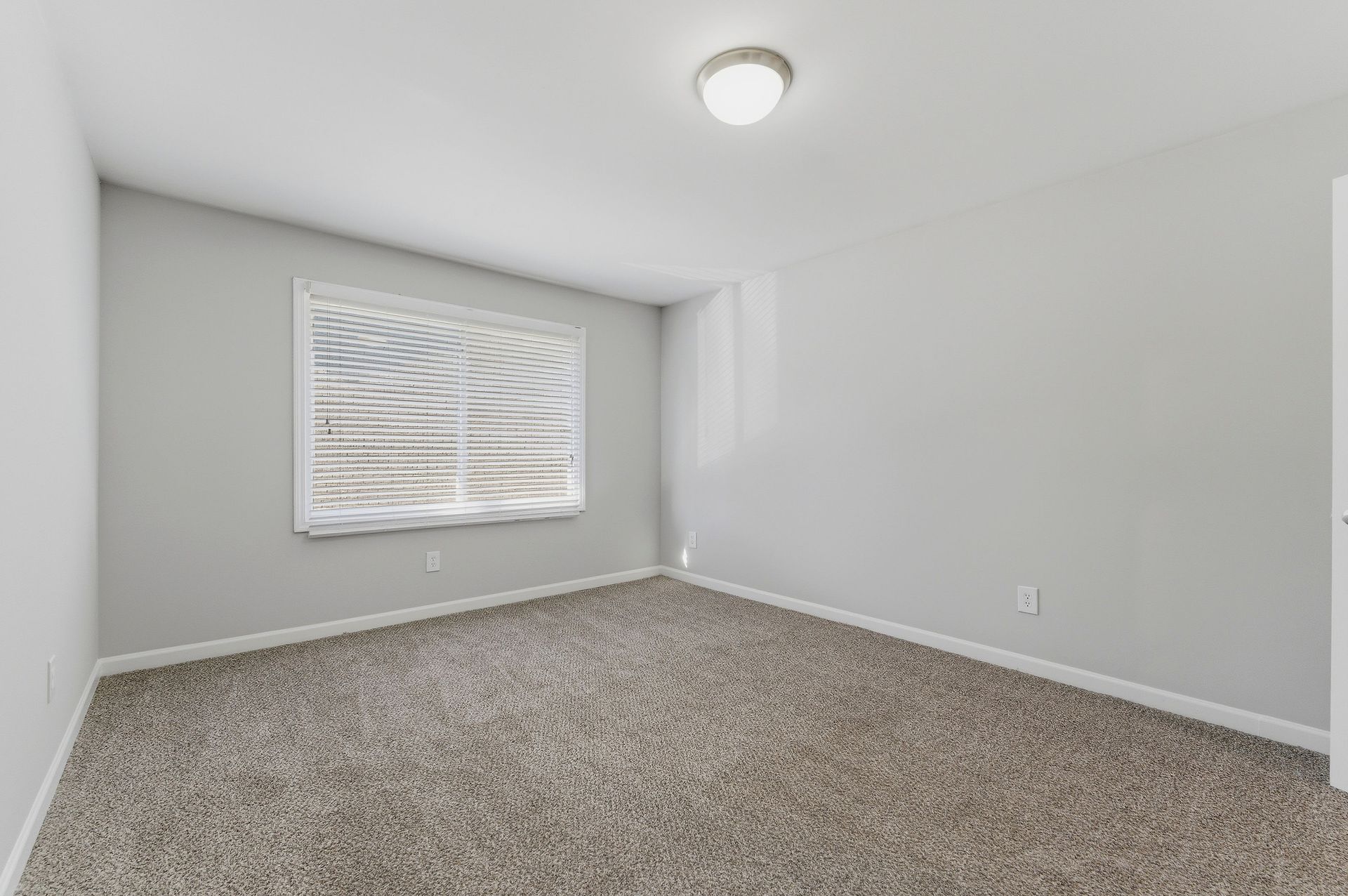Empty gray bedroom with carpet, white walls, and a window with blinds.