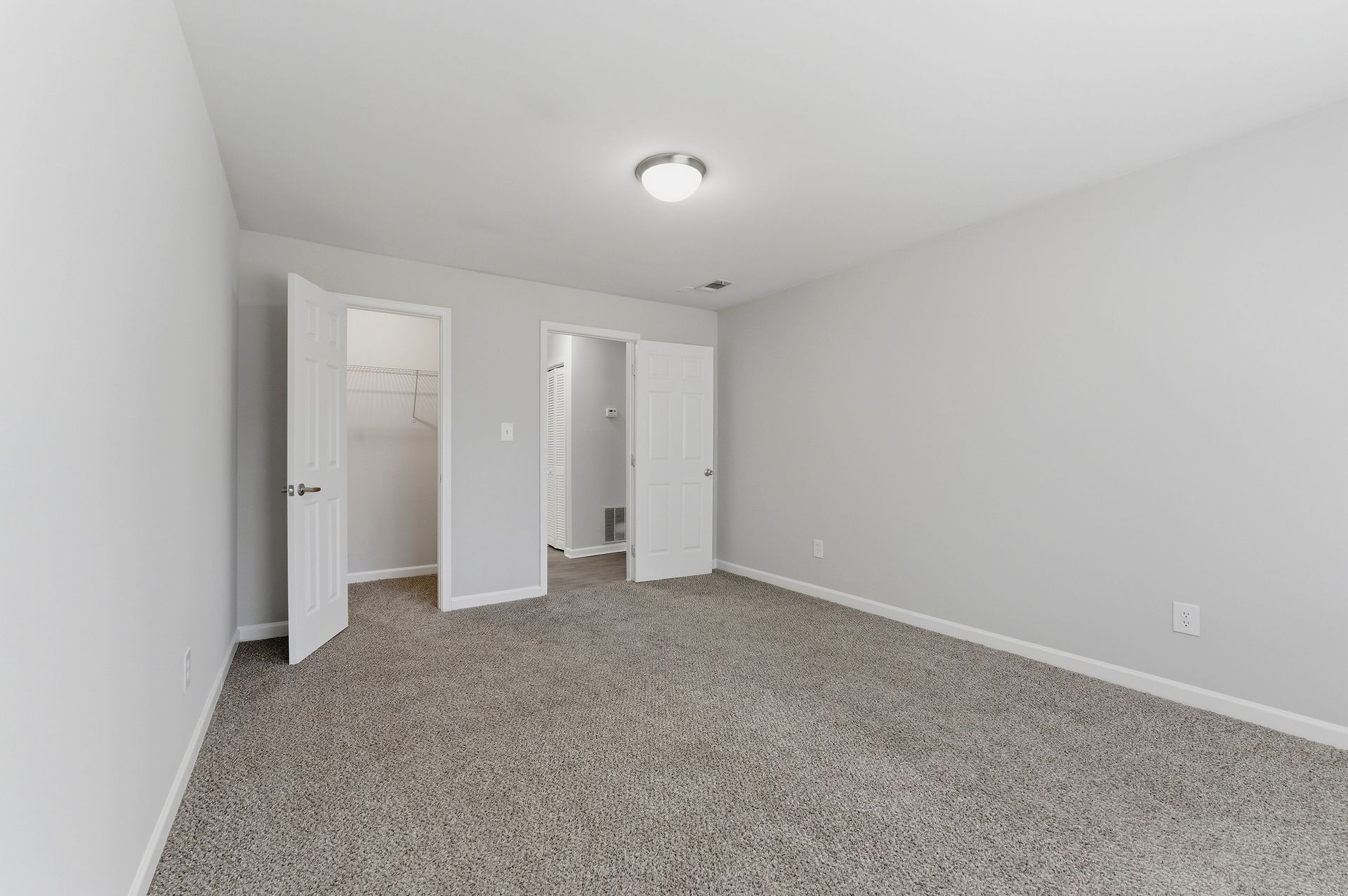 Empty carpeted bedroom with white walls, closet doors, and a ceiling light.