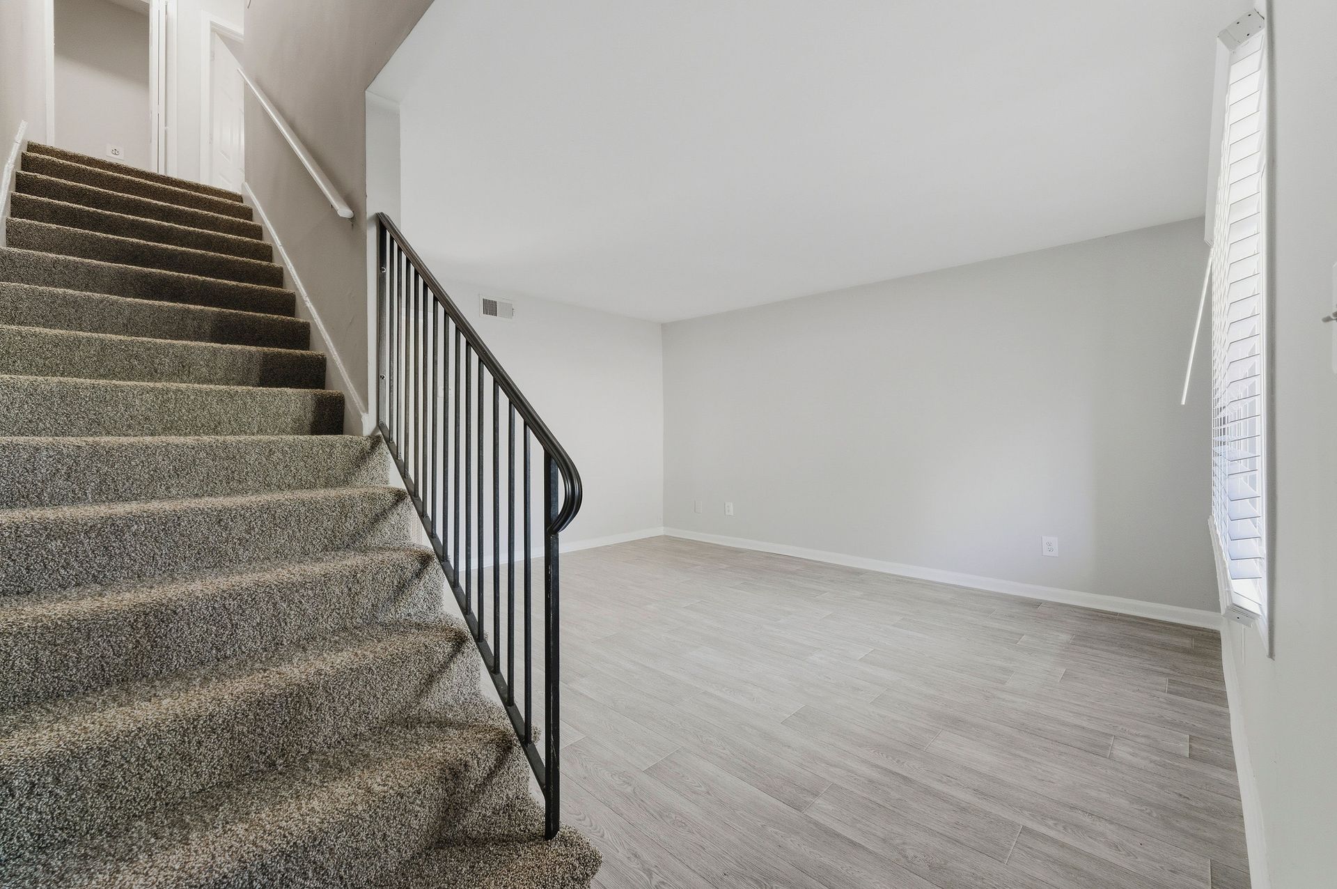 Empty carpeted living room with staircase and black railing at left