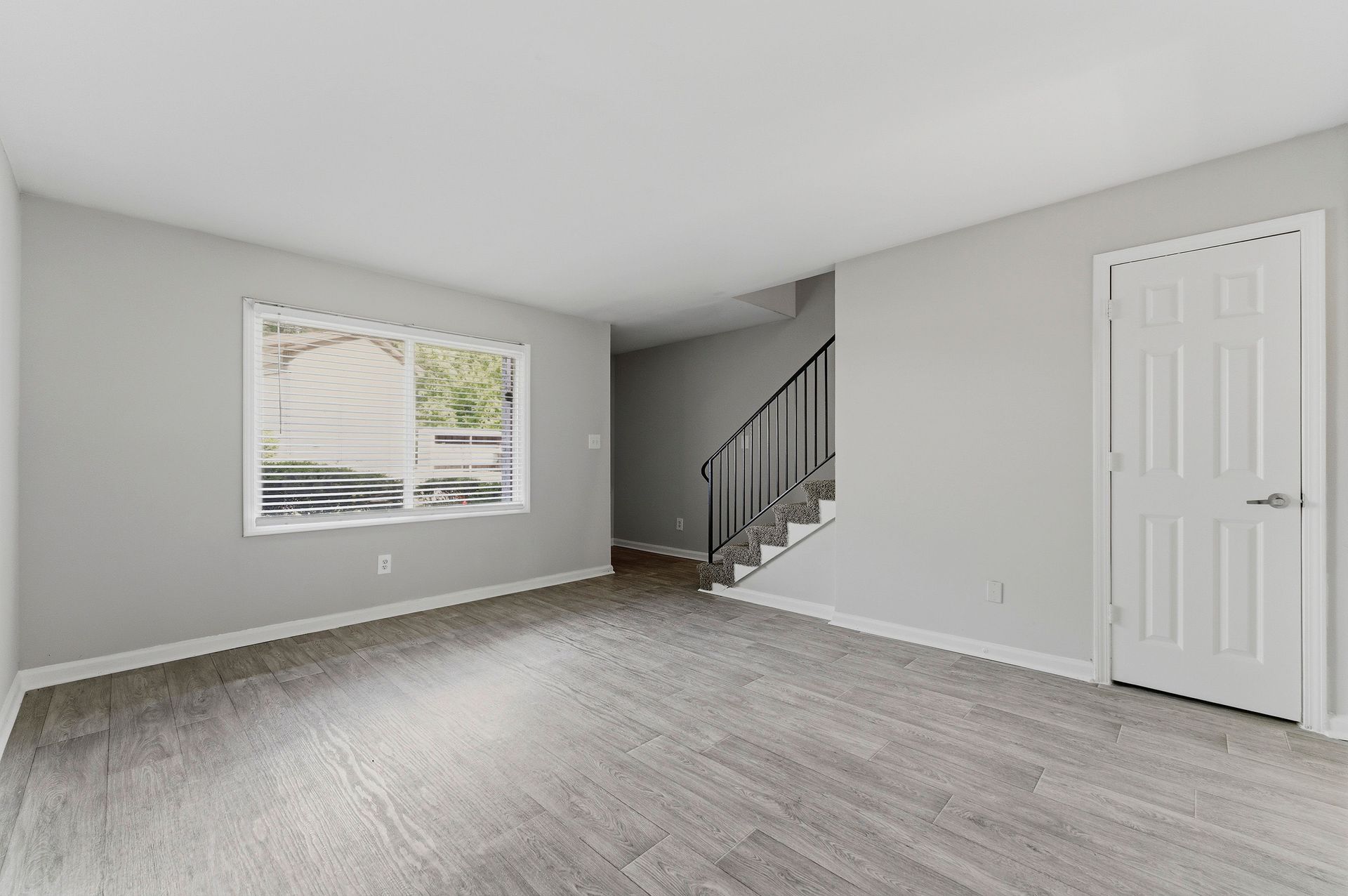 Empty gray living room with a window, wood-look floor, staircase, and white closet door