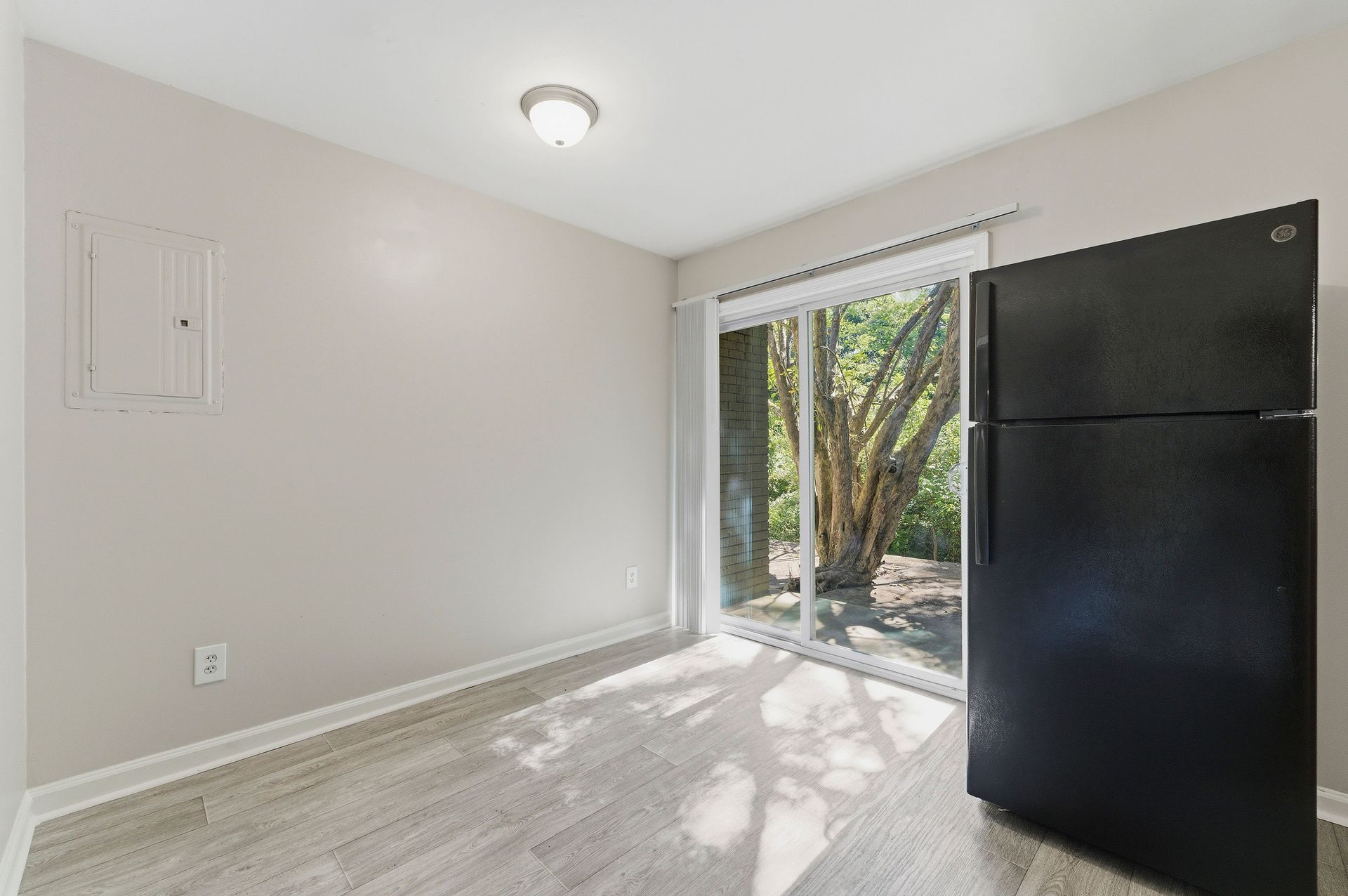 Empty room with white walls, carpet, sliding glass door, and a black refrigerator by the window