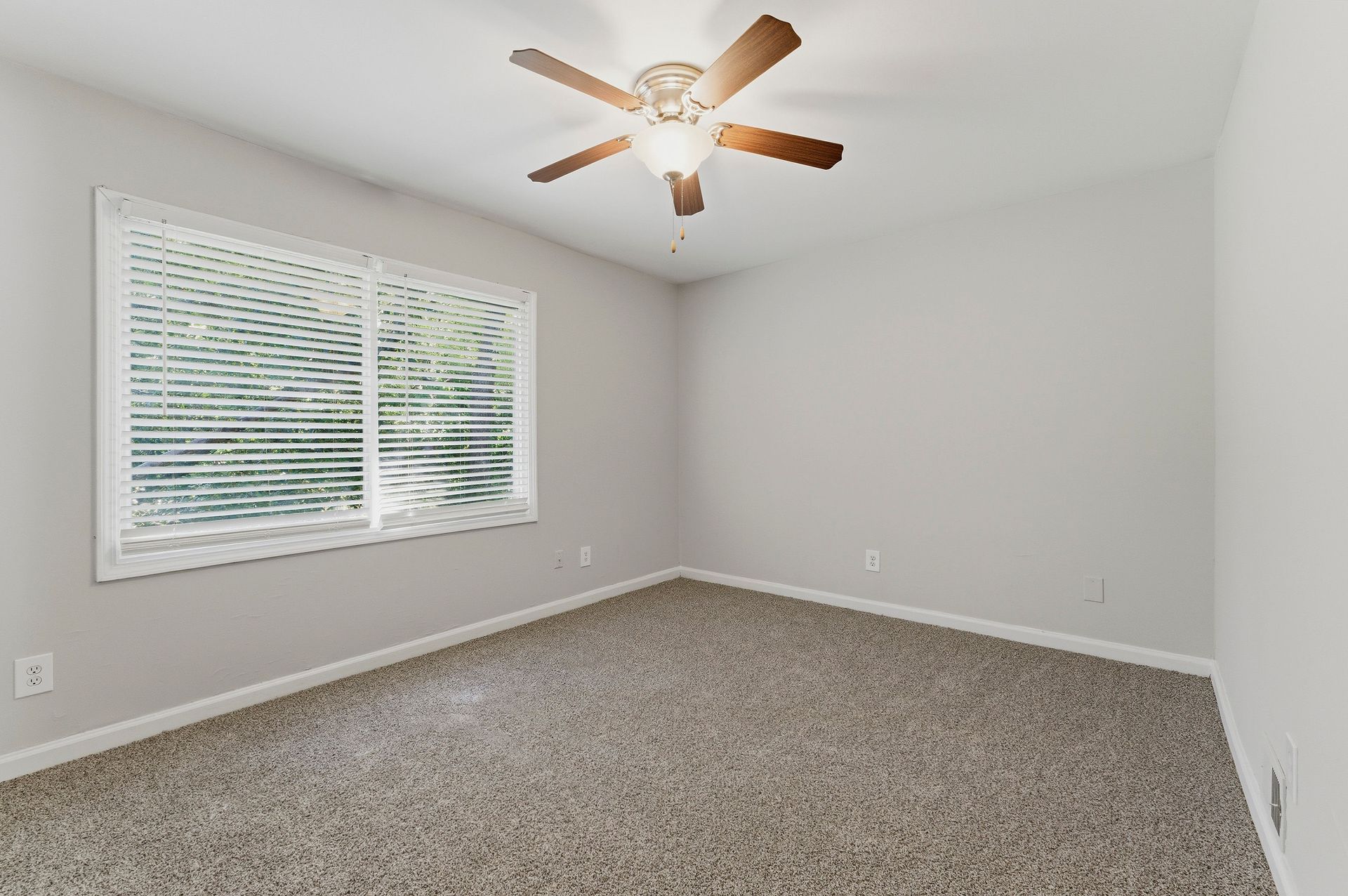 Empty carpeted bedroom with gray walls, white blinds, and a ceiling fan with lights