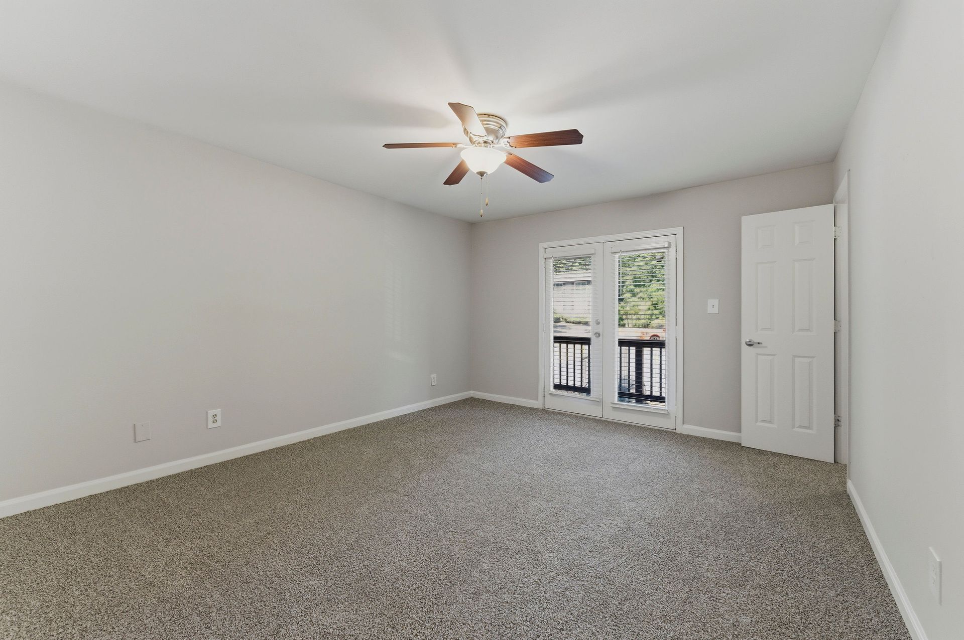 Empty carpeted bedroom with white walls, ceiling fan, closet, and balcony doors