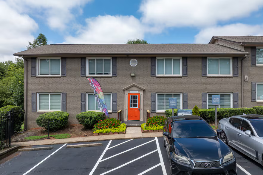 Two-story brick apartment building with parked cars and an American flag by the orange front door