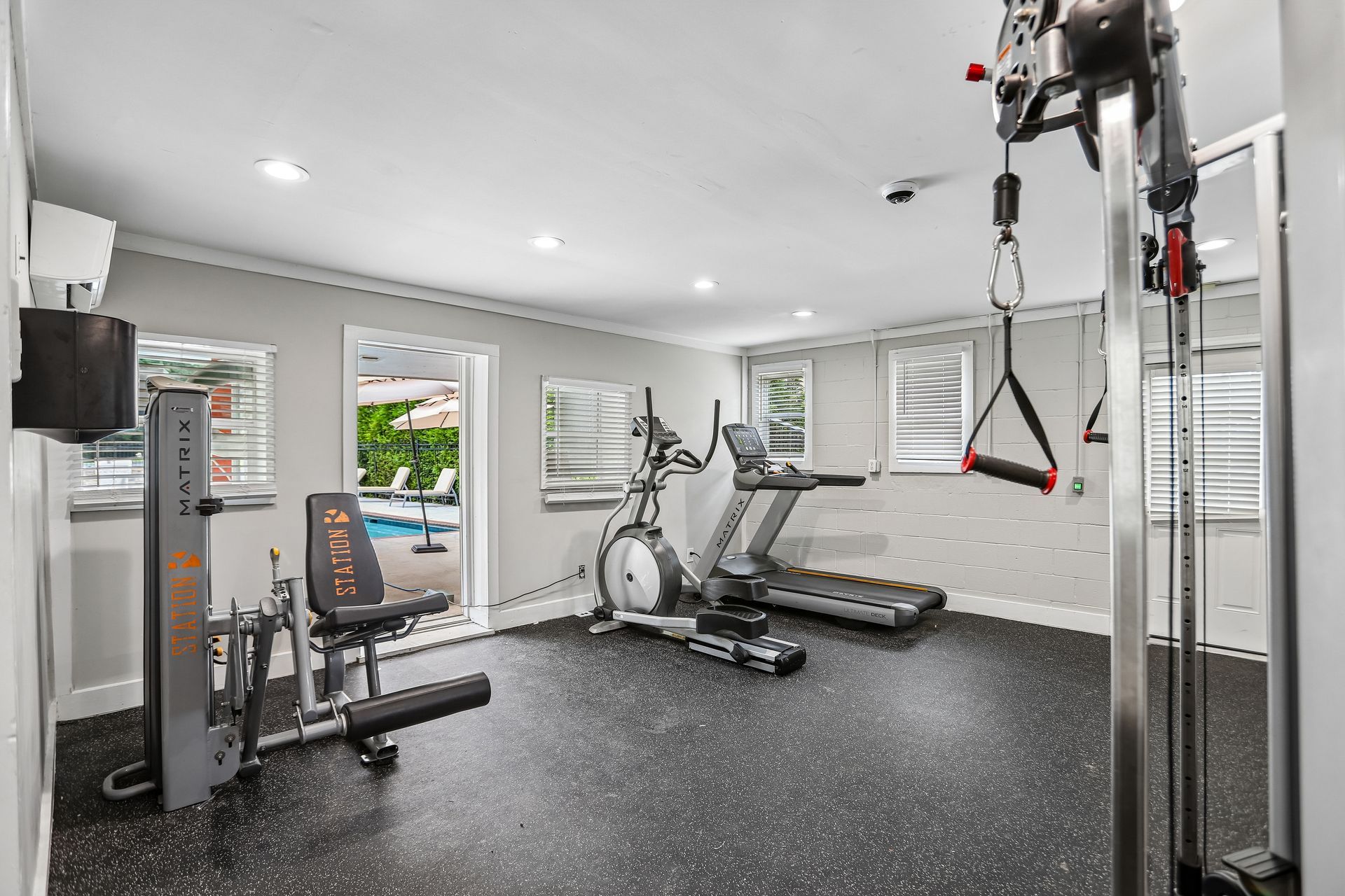 Home gym with treadmill, exercise bike, weights, and cable machine in a bright room