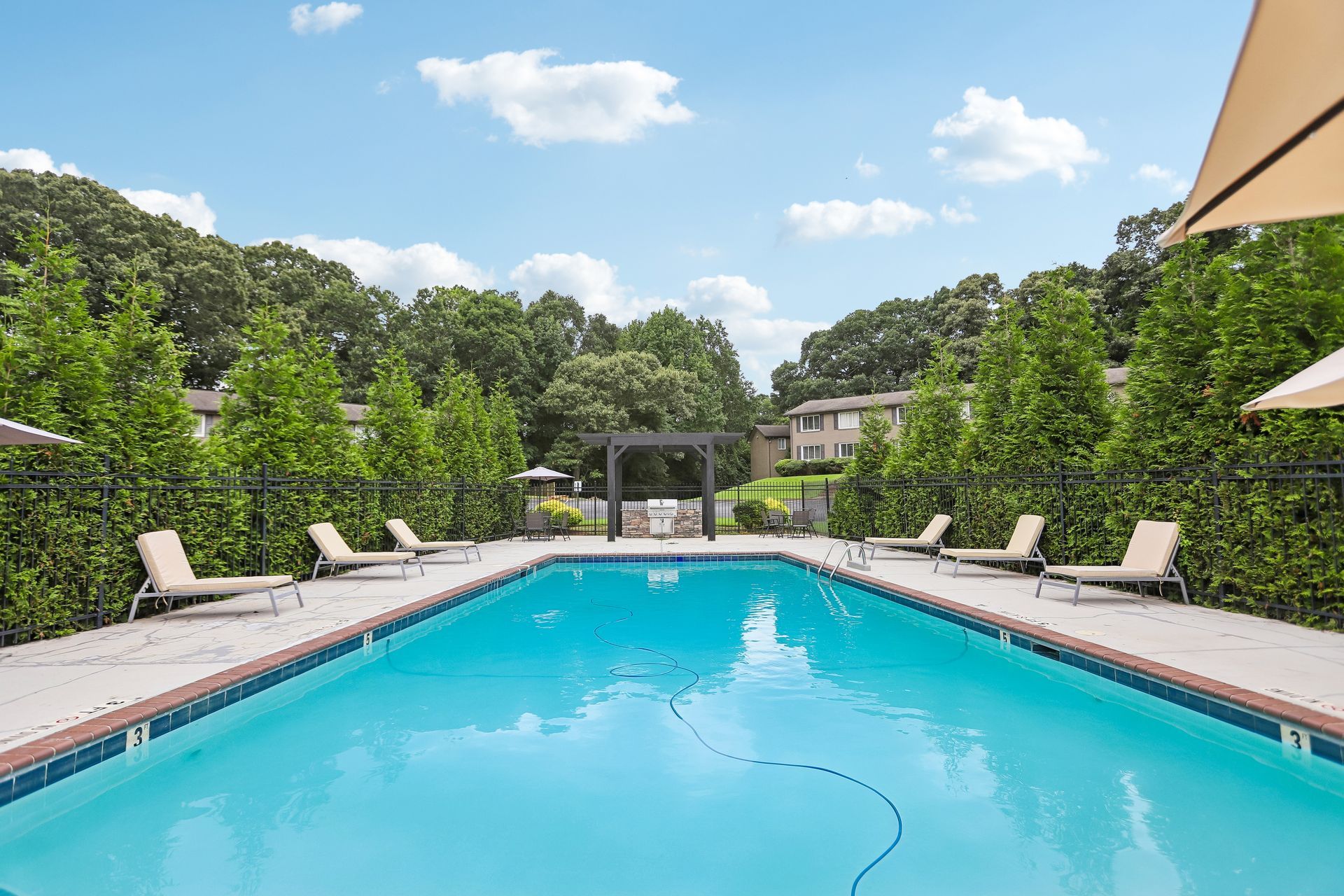 Outdoor swimming pool with turquoise water, lounge chairs, and green hedges under a blue sky
