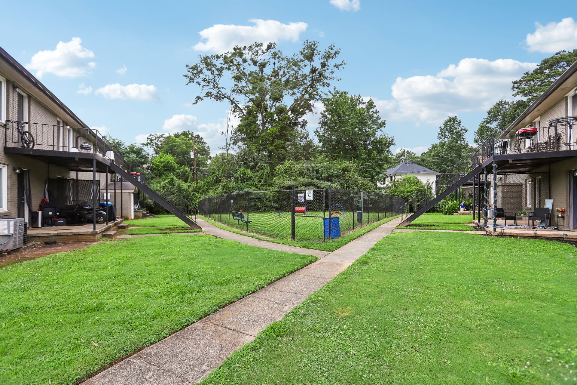 Apartment courtyard with green lawn, central walkway, trees, and buildings on both sides