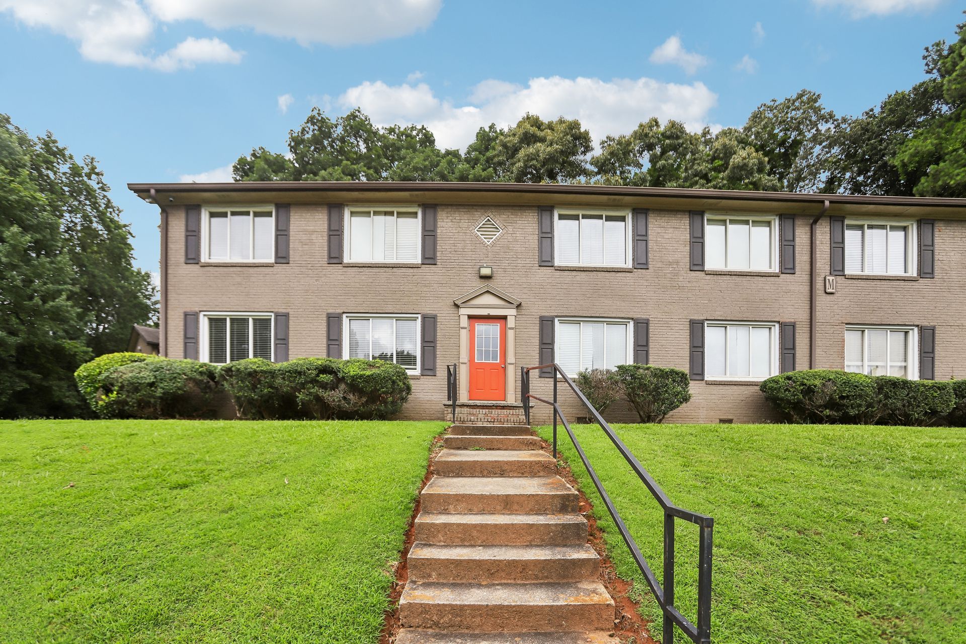 Two-story apartment building with a red front door, brick steps, and a green lawn
