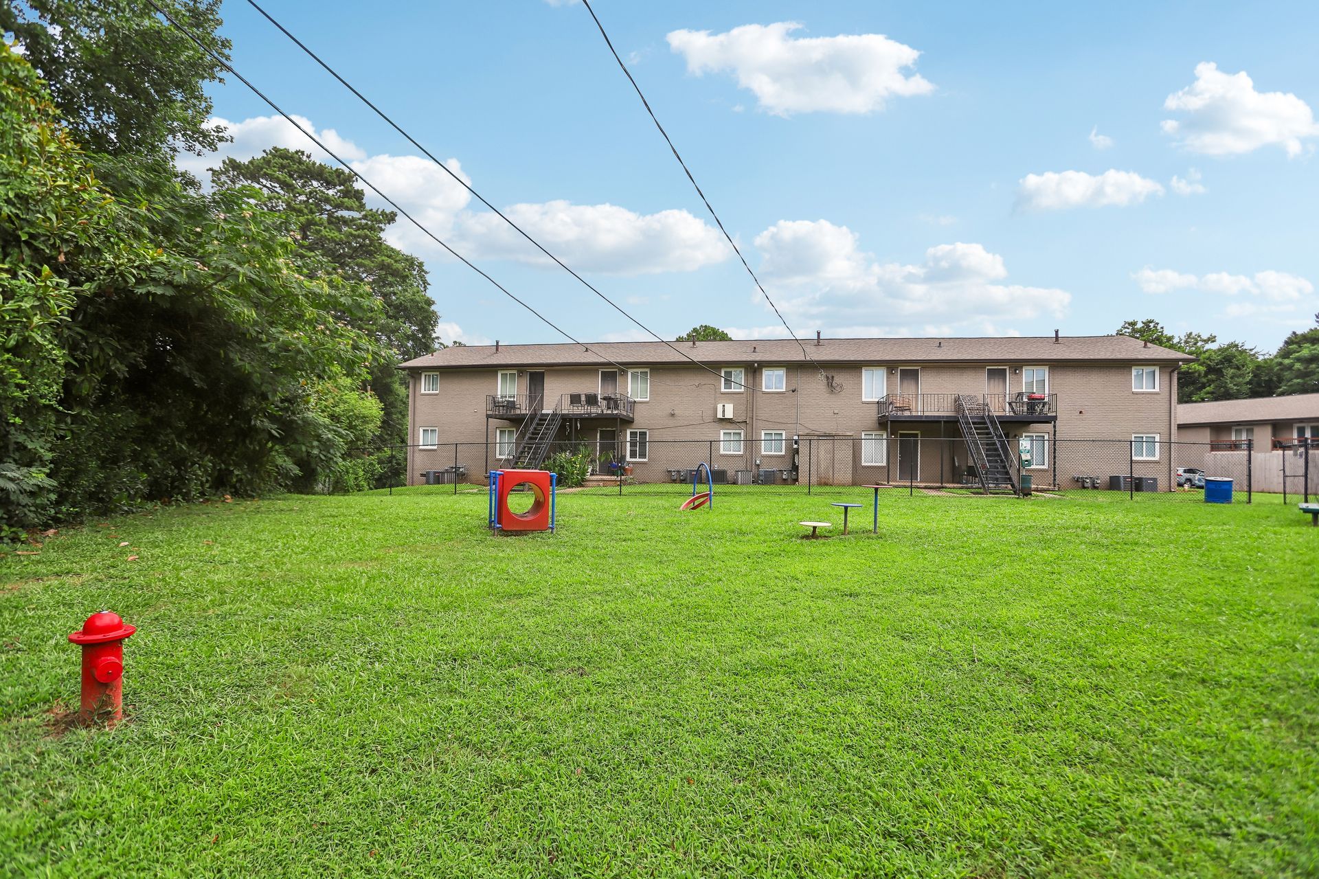 Grassy backyard with a red hydrant, a target stand, and apartment buildings under a blue sky