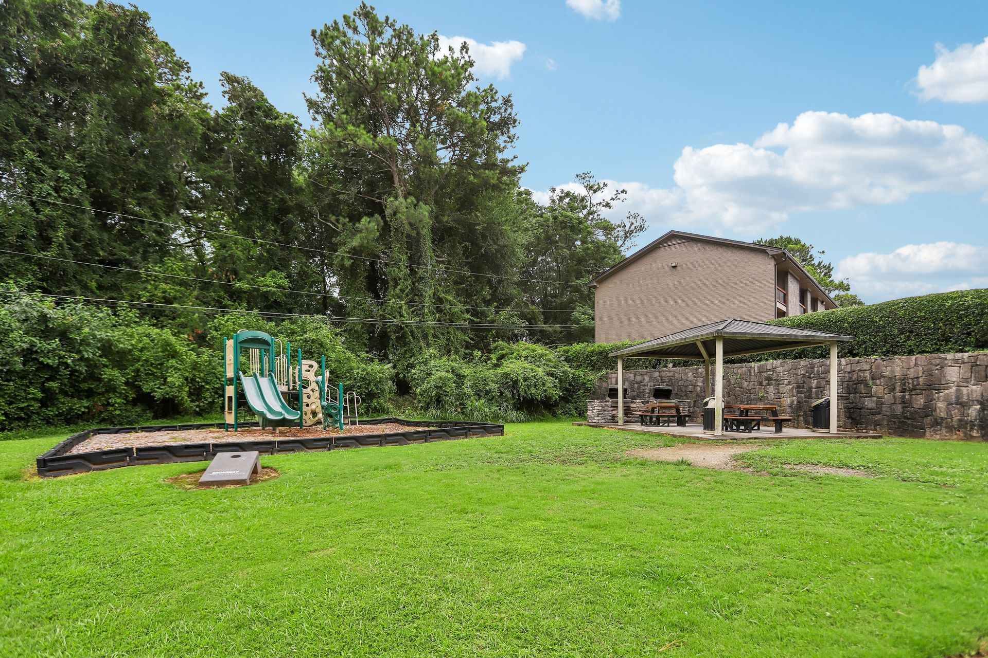 Backyard with green lawn, play structure, and house with patio pergola under a blue sky