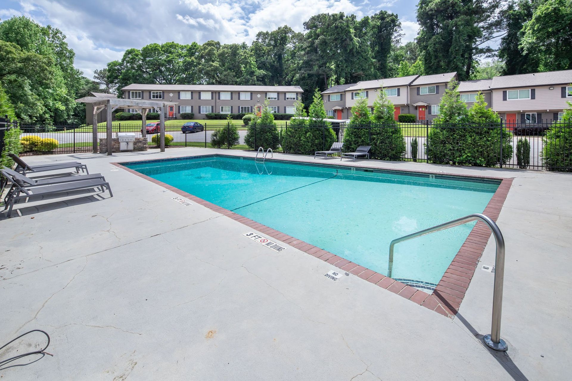 Outdoor apartment pool with turquoise water, lounge chairs, and trees surrounding the deck