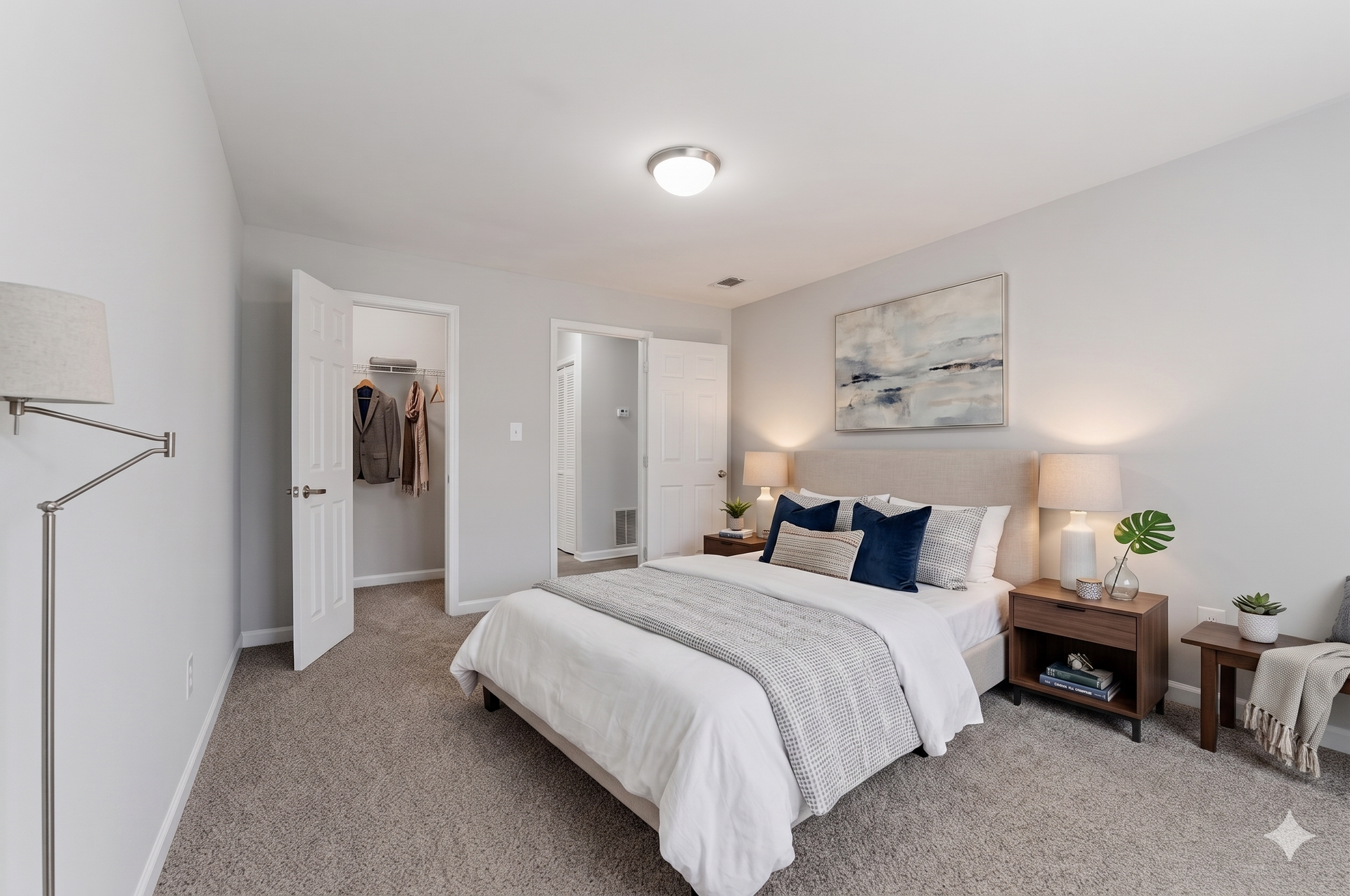 Bright bedroom with white bedding, gray carpet, mirrored closet doors, and a bedside lamp.