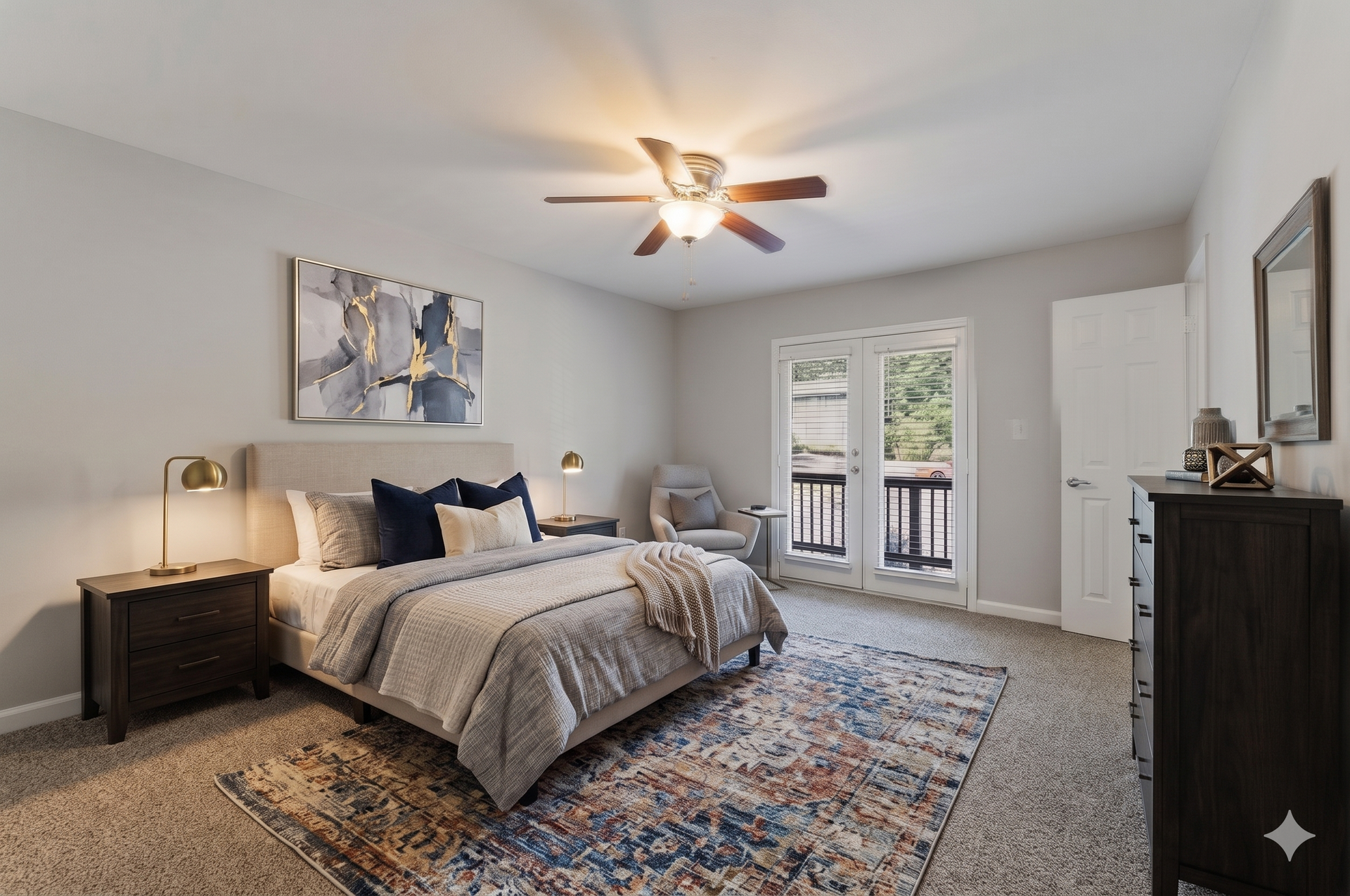 Spacious gray bedroom with a bed, nightstands, ceiling fan, rug, and French doors to a balcony.