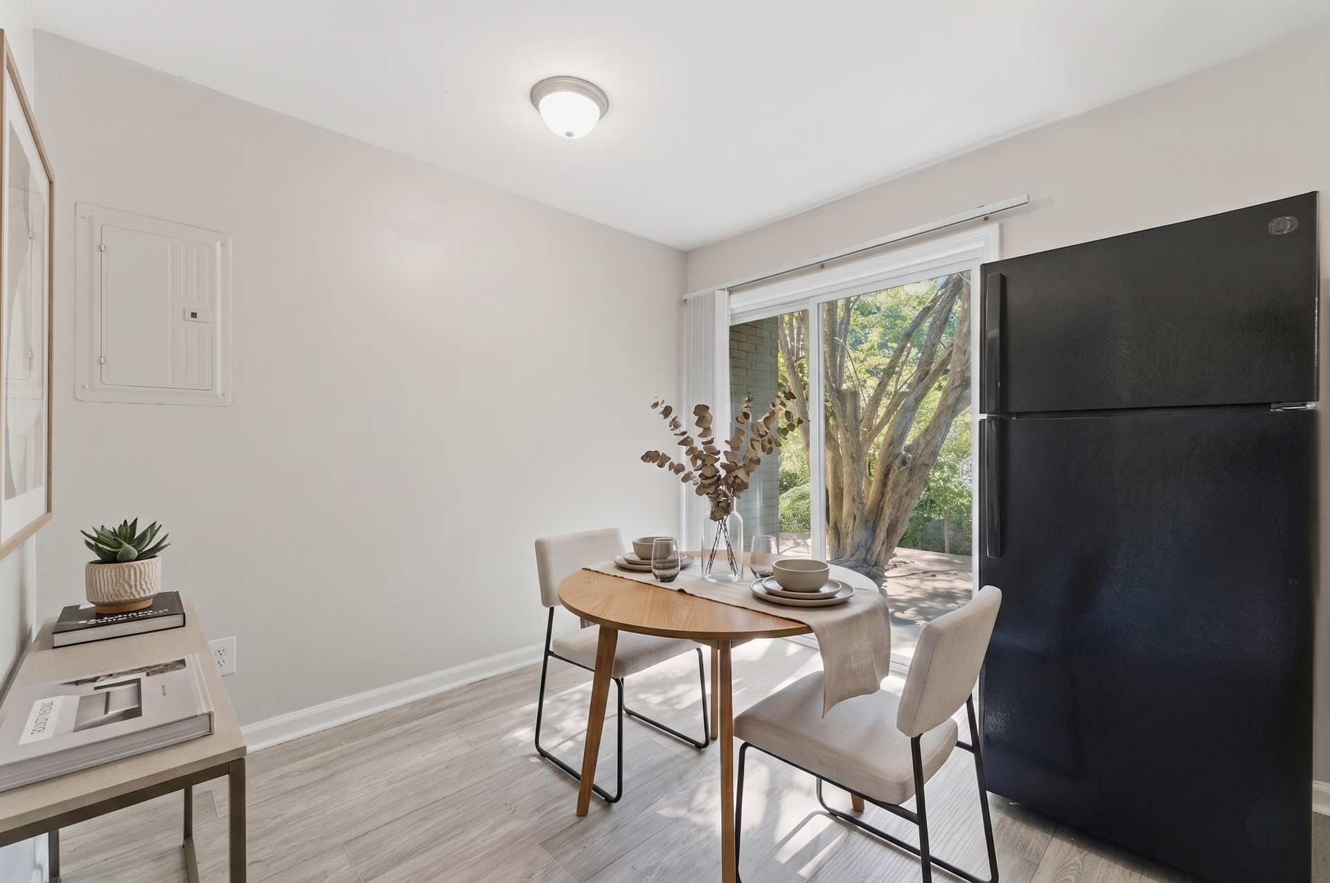 Bright dining nook with table and chairs beside a black refrigerator and sliding glass door