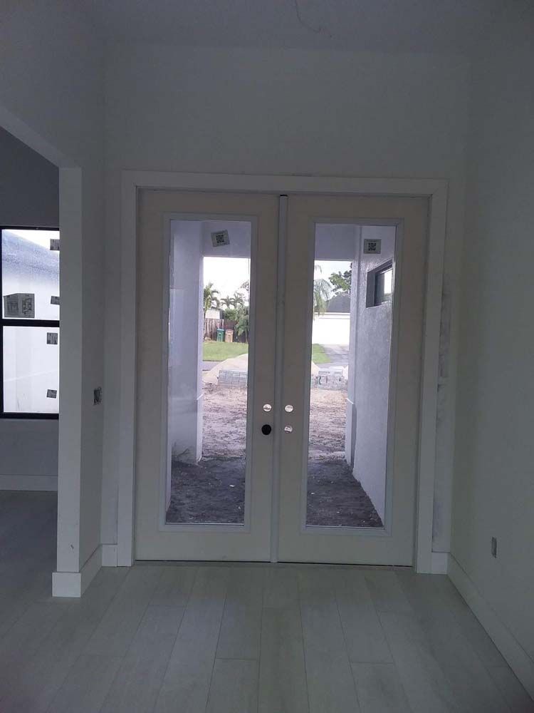 Double white glass doors in a light-filled room, leading outside to a walkway and green space.