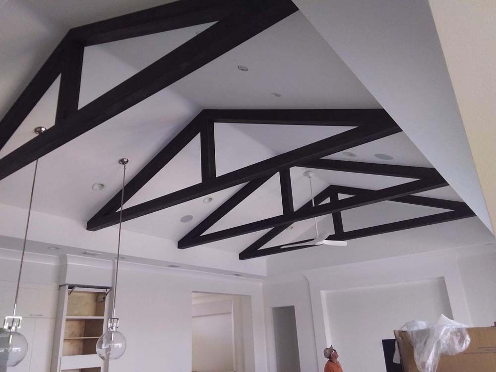 Black wooden beams form a geometric pattern on a white ceiling, creating a modern architectural design.