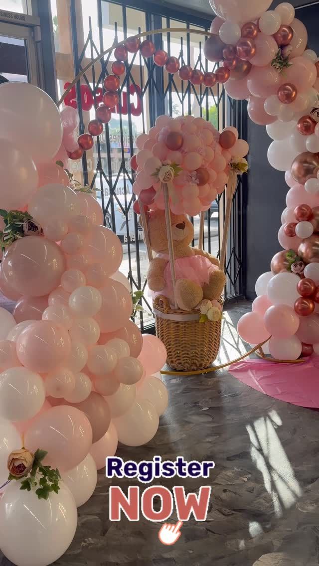 Arco de globos de color rosa y blanco con un osito de peluche en un arreglo floral; superposición de texto 