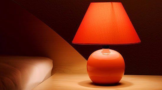 Orange ceramic table lamp on bedside table; The Shade Tree in Houston, TX