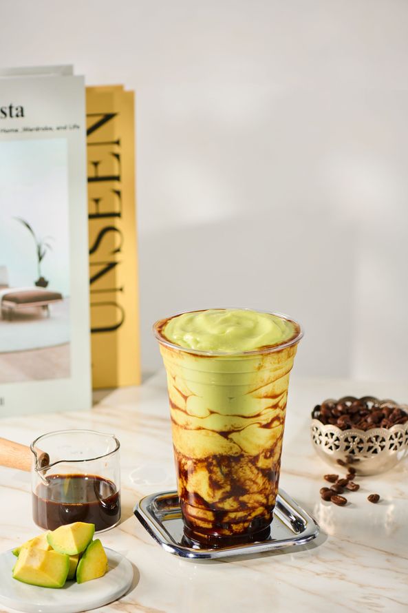 Iced matcha drink in a patterned glass with lime dessert and a small tea cup on a bright table