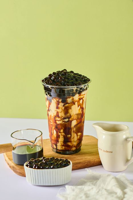 Fruit parfait in a glass with granola and berries, surrounded by small bowls and a white pitcher on a wood tray.