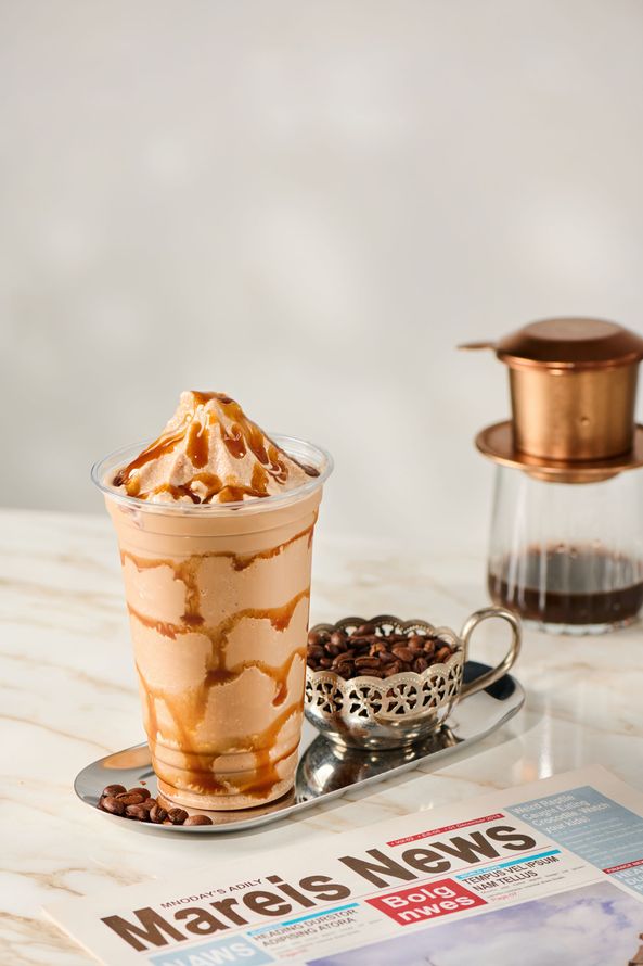 Coffee glass with caramel drizzle, chocolate sprinkles, and a Turkish coffee pot beside a newspaper.
