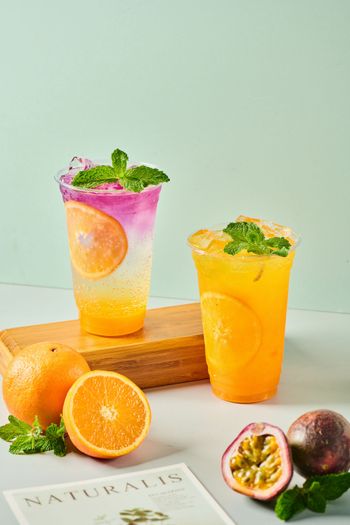 Two colorful passion fruit cocktails with mint and orange slices on a light green background