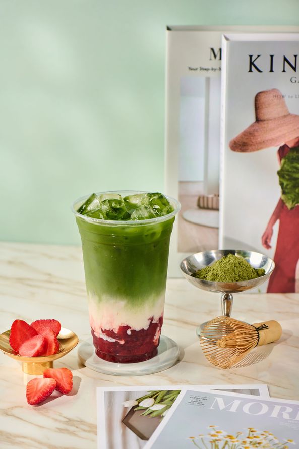 Green layered smoothie in a glass with strawberries on a marble table, with books and a spoon nearby