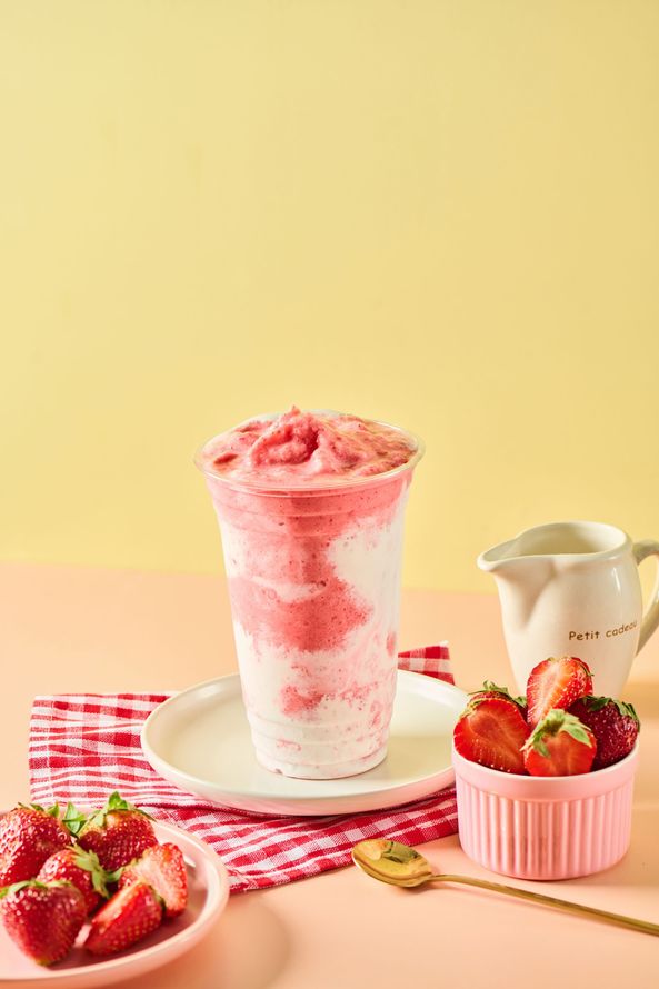 Strawberry milkshake in a glass with fresh strawberries and a pitcher on a pink checkered cloth