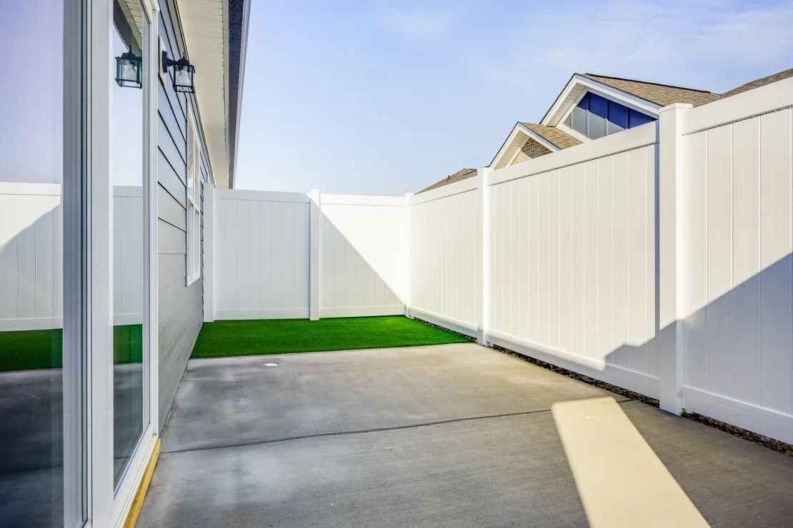 A white vinyl fence surrounds a concrete walkway leading to a house.