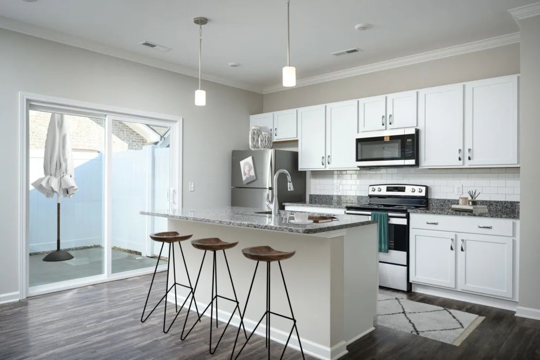 A kitchen with white cabinets , stainless steel appliances , a refrigerator , microwave , and stools.