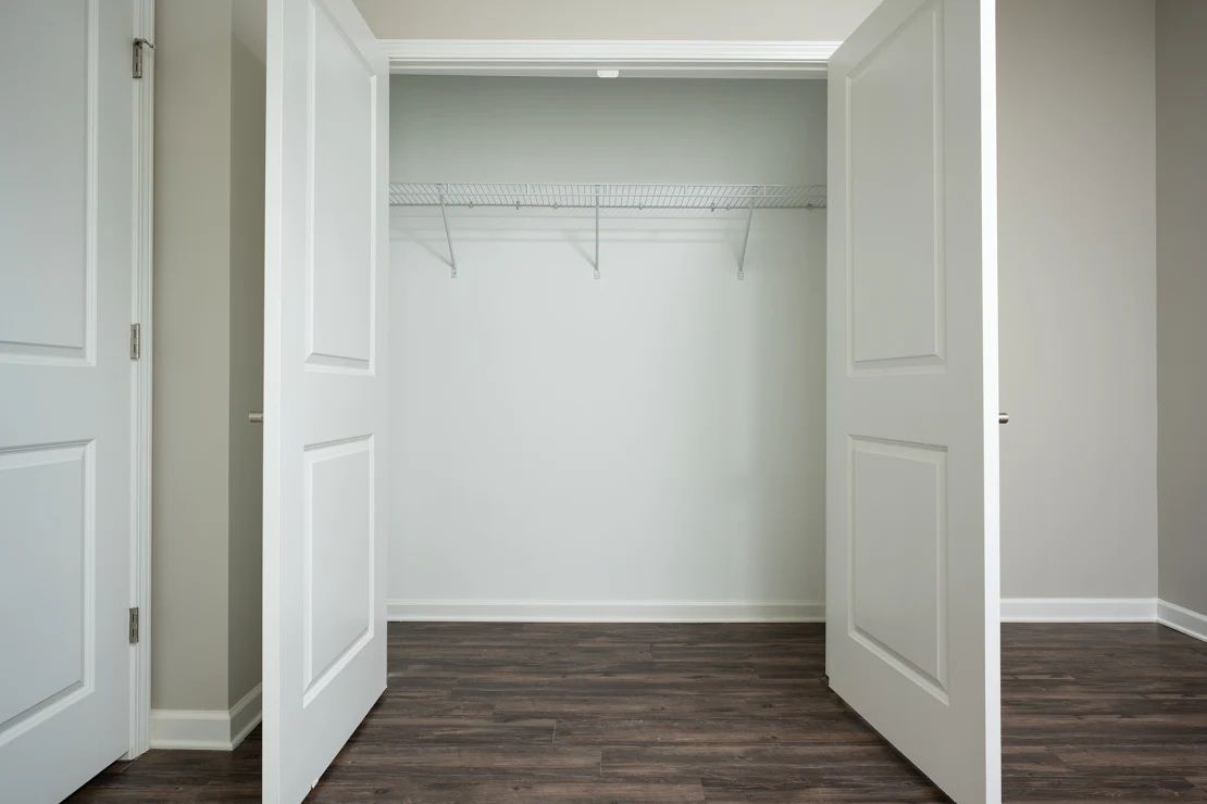 An empty closet with the doors open and a wooden floor.