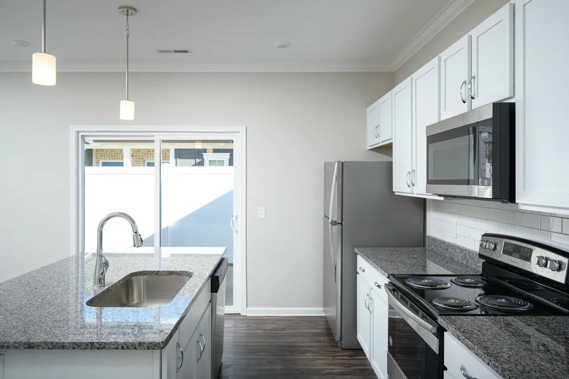 An empty kitchen with granite counter tops , stainless steel appliances , and white cabinets.