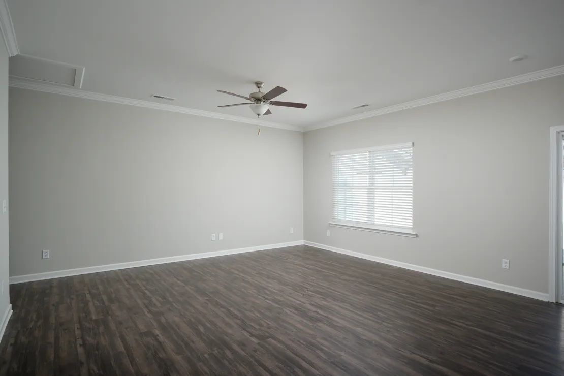 An empty living room with a ceiling fan and a window.