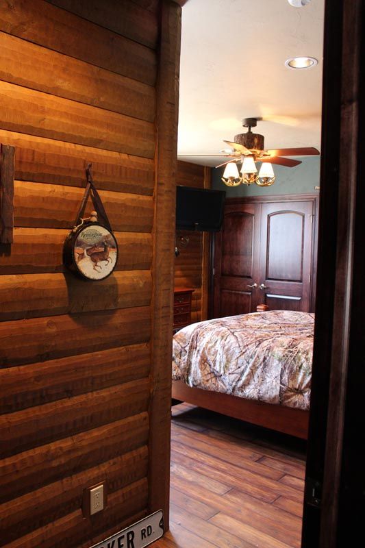 Wood-paneled hallway opening into a bedroom with a wood floor, bed, ceiling fan, and warm lighting.