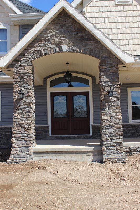 Front entrance of a house with stone columns, arched porch, and double wooden doors.