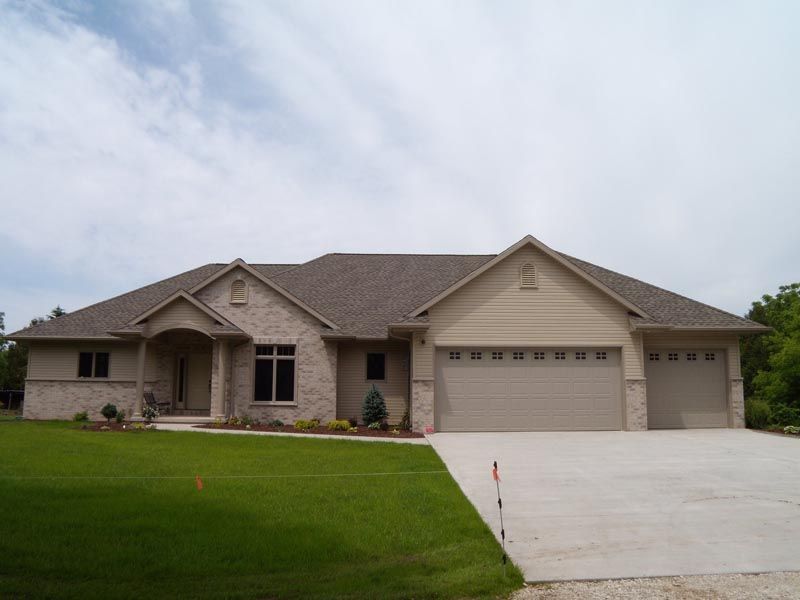 Single-story suburban house with beige siding, a two-car garage, and a large green lawn.