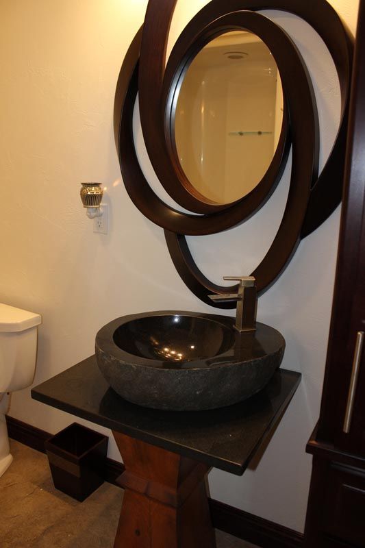 Modern bathroom vanity with round vessel sink, dark wood table, and circular mirror above.