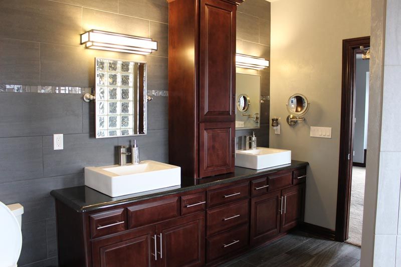 Modern bathroom with dark wood double vanity, white sinks, mirrors, and gray tiled walls