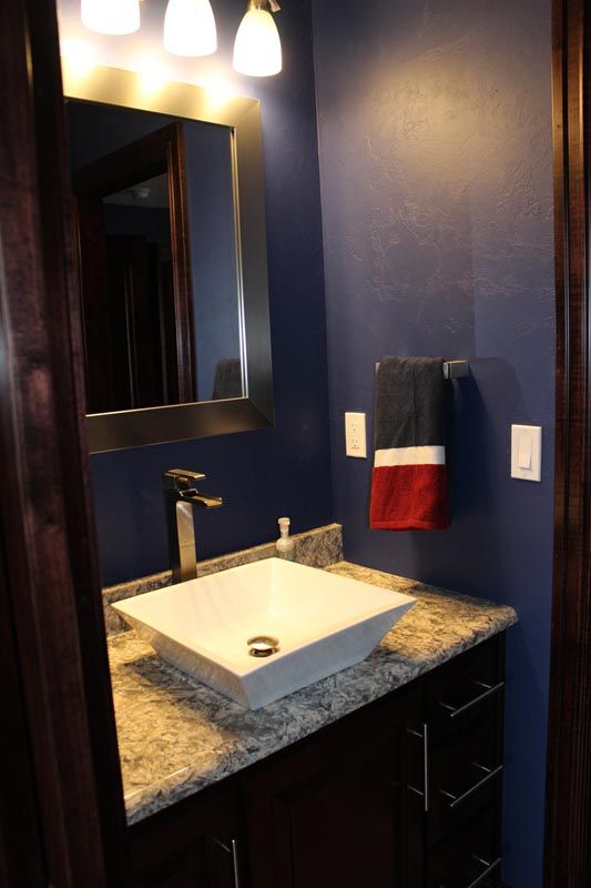 Small bathroom vanity with sink, mirror, and dark blue walls, lit by two wall sconces.