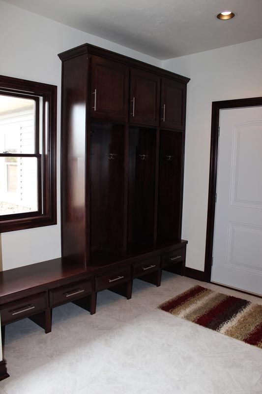 Dark wood hall tree with bench and coat hooks in a white entryway, next to a door and window.