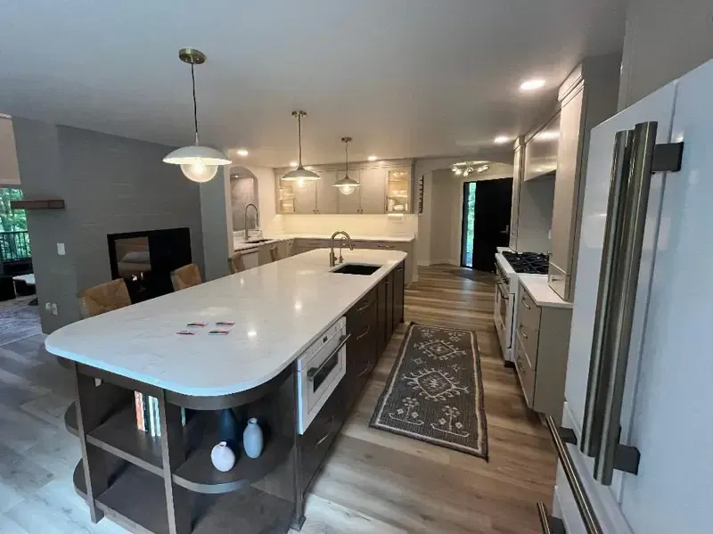 Modern kitchen with large island, pendant lights, white cabinets, and a hallway rug leading to the back door