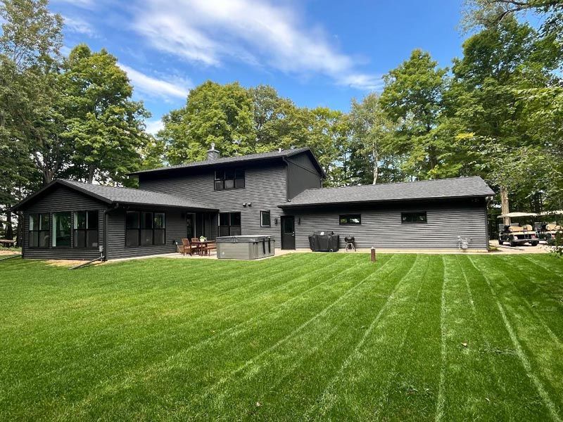 Modern dark gray house with a wide green lawn and trees under a blue sky