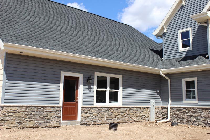 House exterior with gray siding, stone foundation, and a wooden front door under a cloudy sky