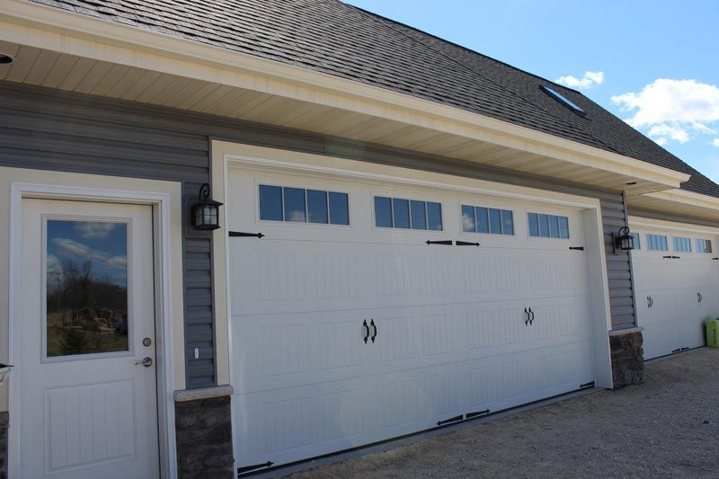 Suburban garage with white doors, gray siding, and a front entry door under a shingled roof