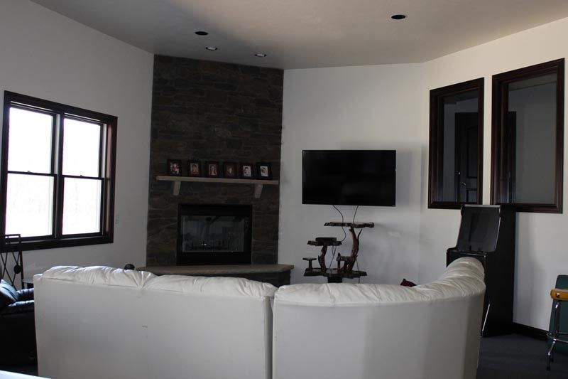 Modern living room with white sectional sofa, wall-mounted TV, fireplace, and large windows