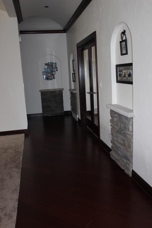 Long hallway with dark wood floor, white walls, stone accents, and glass doors on the right