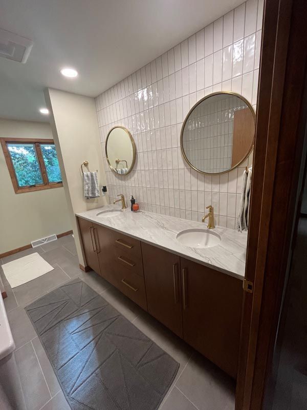 Modern bathroom with dark wood vanity, double sinks, round mirrors, and white tile walls